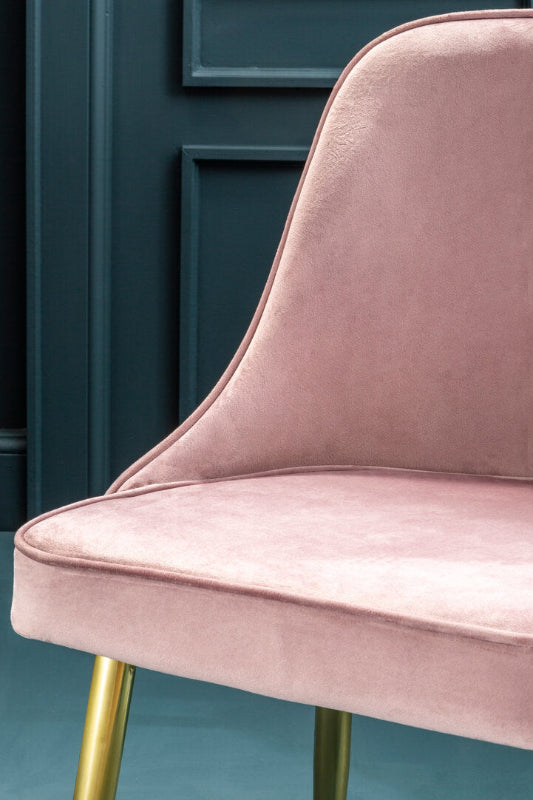 Pink velvet chair with gold legs against a teal wall