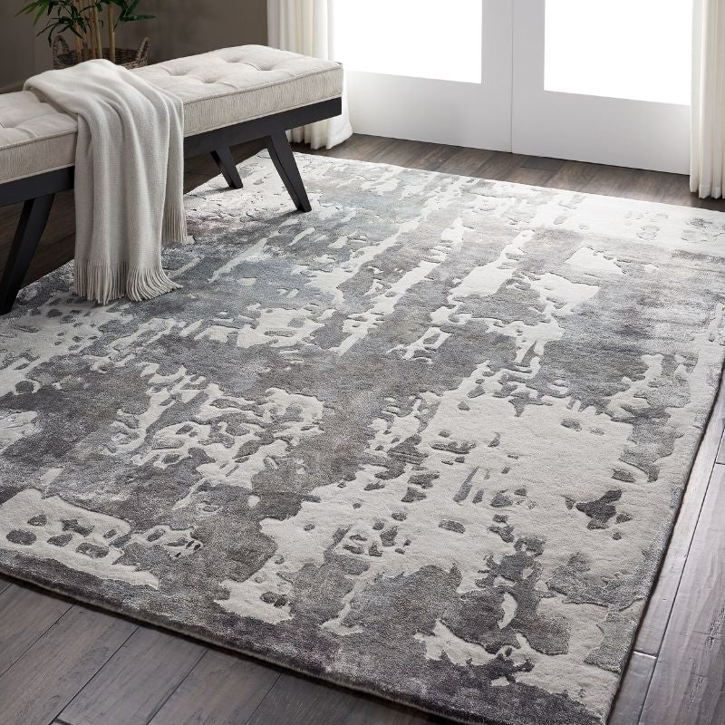 Gray and white patterned rug on a wooden floor with a bench and blanket in the background.