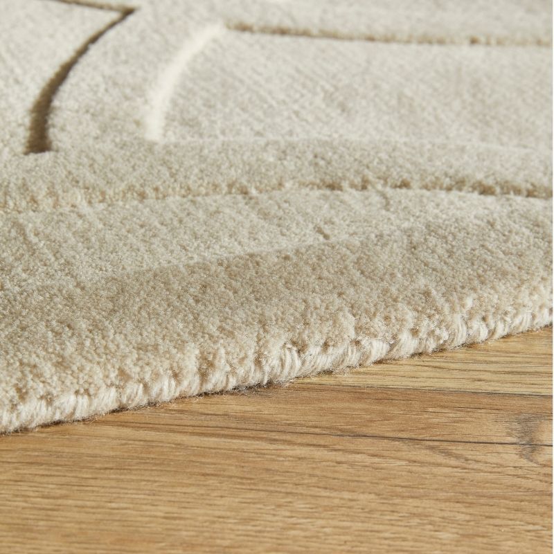 Close-up of a cream-colored textured rug with a raised geometric pattern, shown on a light brown wooden floor.