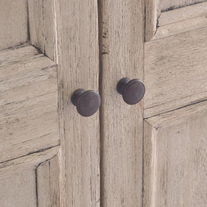 Close-up of a distressed light wood cabinet door with two round dark metal knobs.