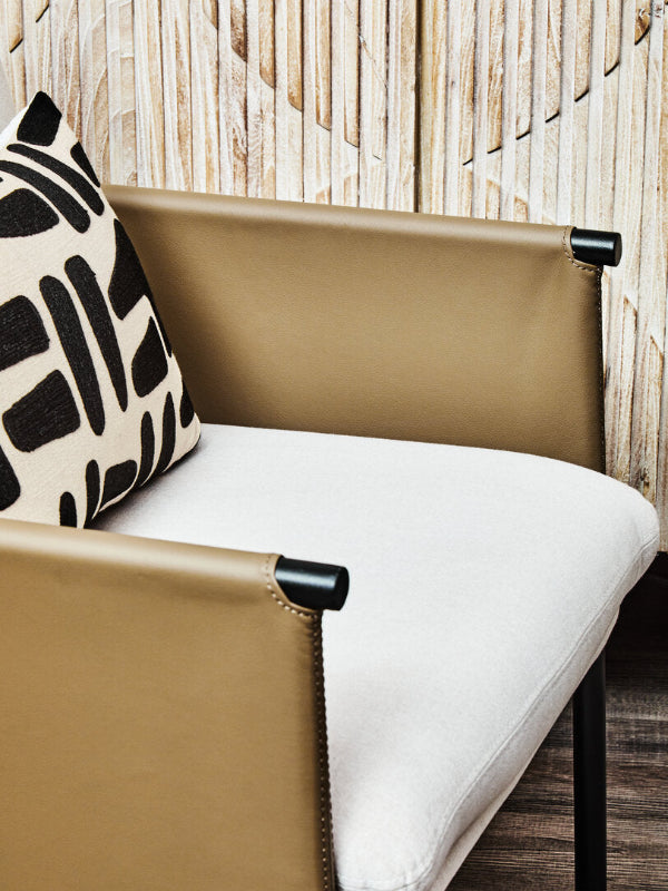 Beige chair with white cushion and black and white patterned pillow against a wooden wall.
