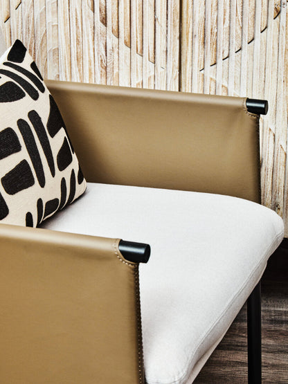 Beige chair with white cushion and black and white patterned pillow against a wooden wall.