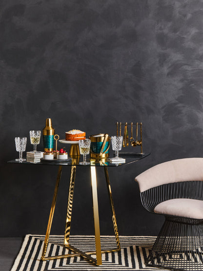 Glass table with decorative items black metal chair with beige cushioning against a dark wall with a striped rug
