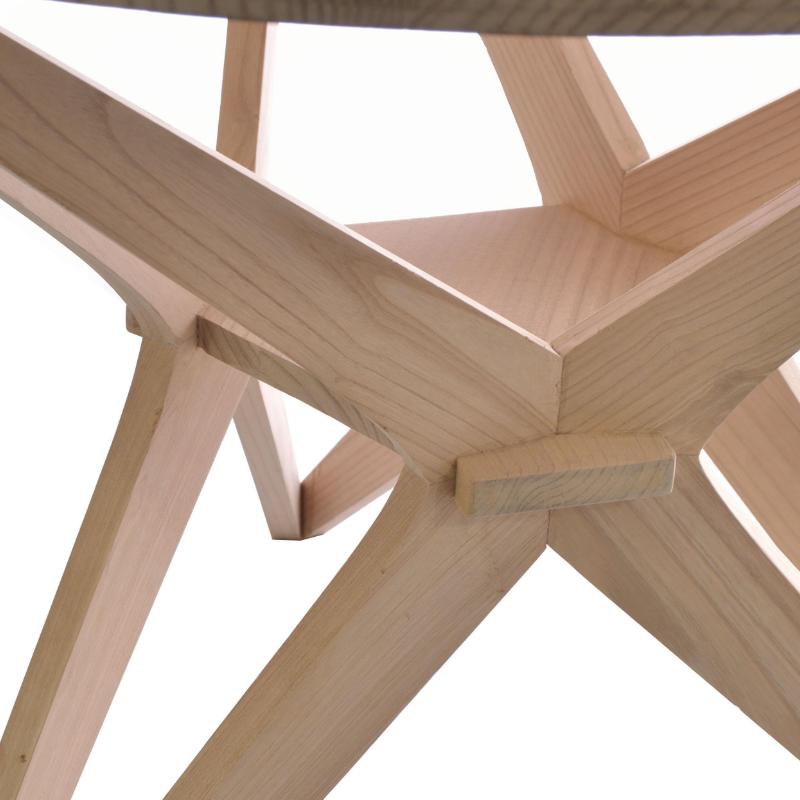 Close-up of a light natural wood table base with geometric star-like intersecting legs and visible wood grain on a white background.