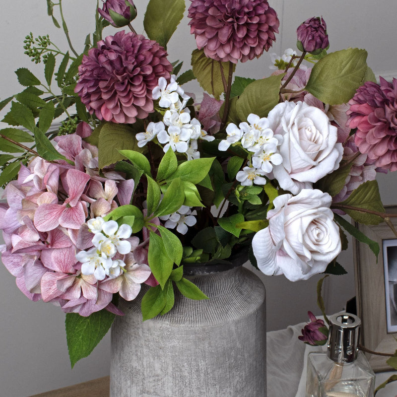 Bouquet of pink, white, and purple flowers in a gray vase against a neutral background.