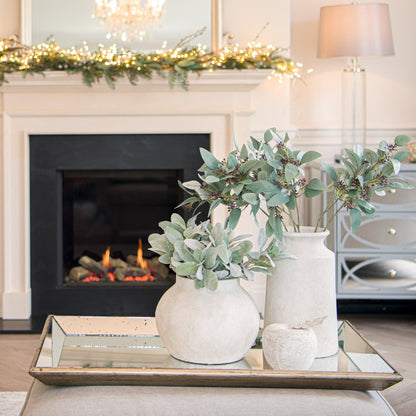 Decorative vases with greenery on a coffee table in front of a fireplace.