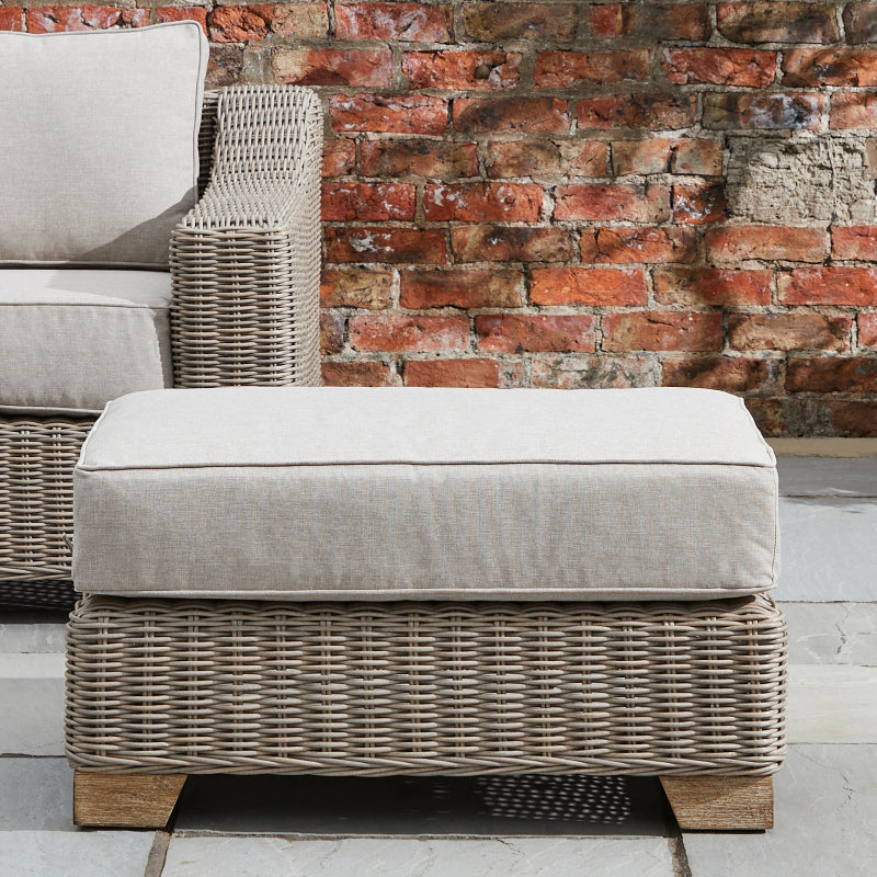 Wicker ottoman with cushion against a brick wall