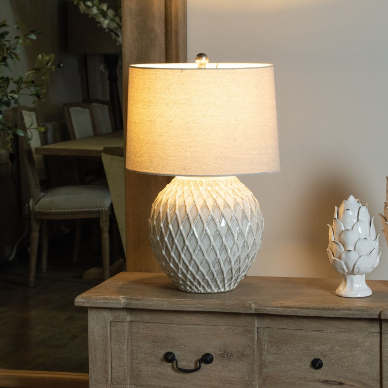 Decorative lamp with textured white base on a wooden cabinet in a home setting