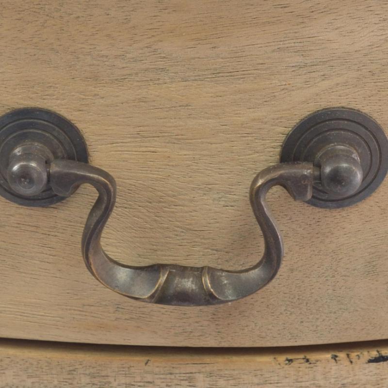 A close-up of a vintage-style metal drawer pull handle mounted on a light wood drawer front.