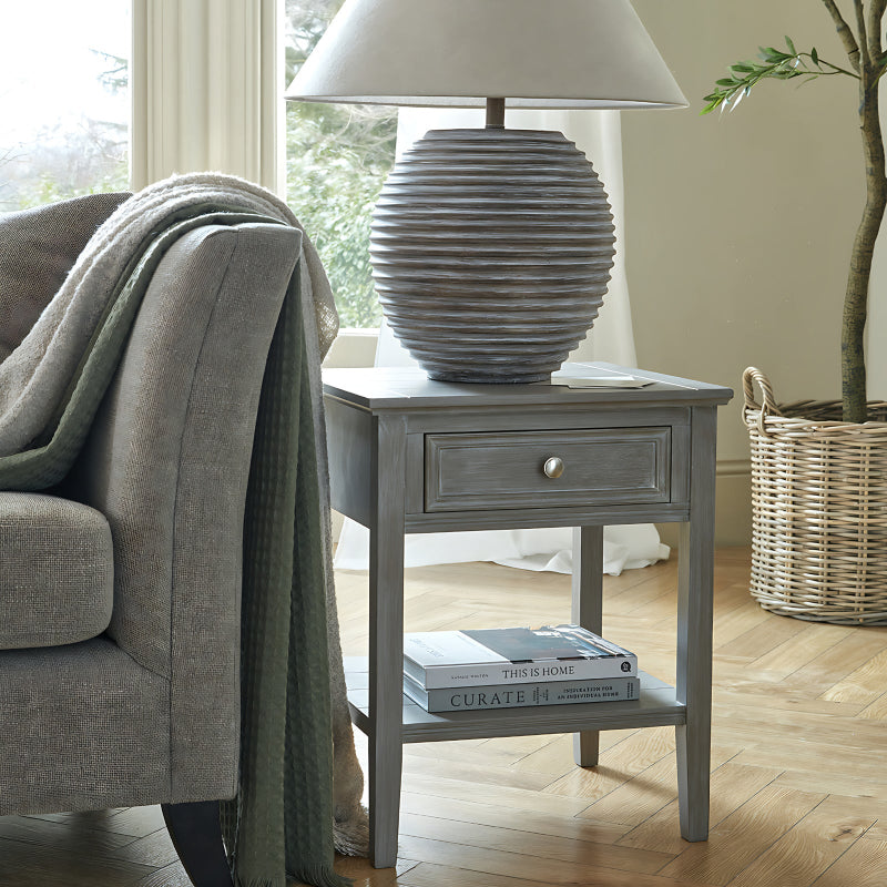 Grey side table with lamp and books next to a gray sofa in a living room.