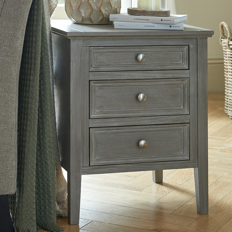 Gray wooden nightstand with three drawers on a wooden floor.