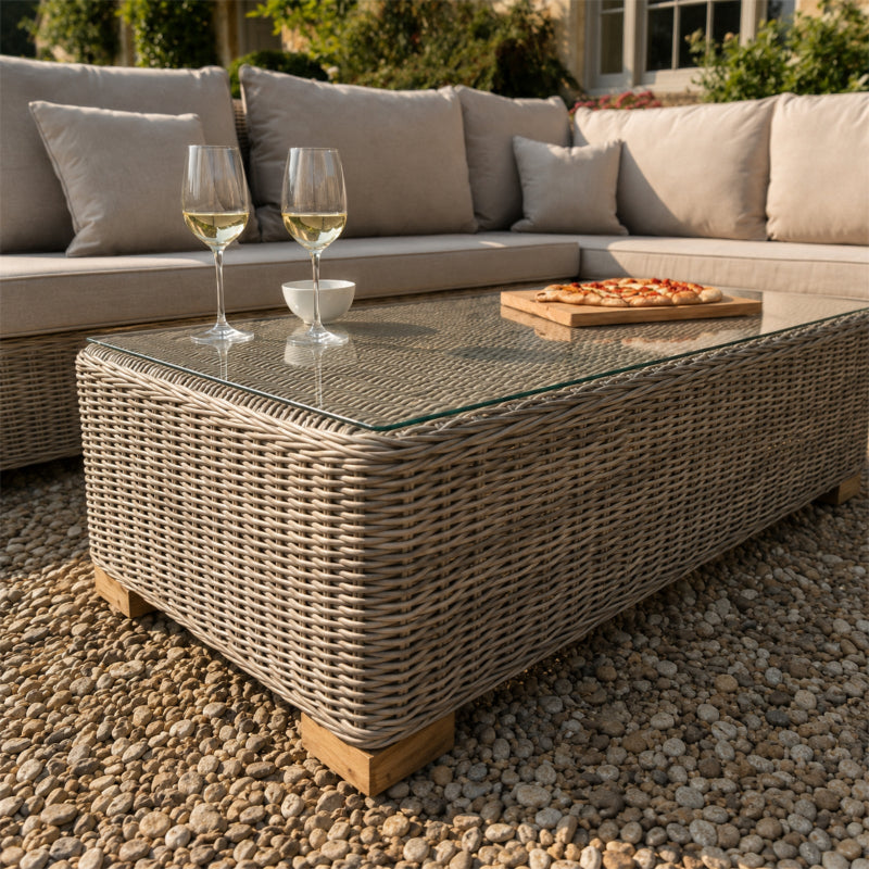 Outdoor patio setting with wicker coffee table, glasses of white wine, and a pizza.