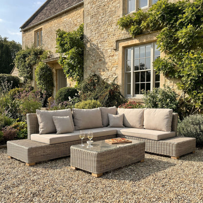 Outdoor patio set with a sectional sofa and coffee table in front of a stone building.