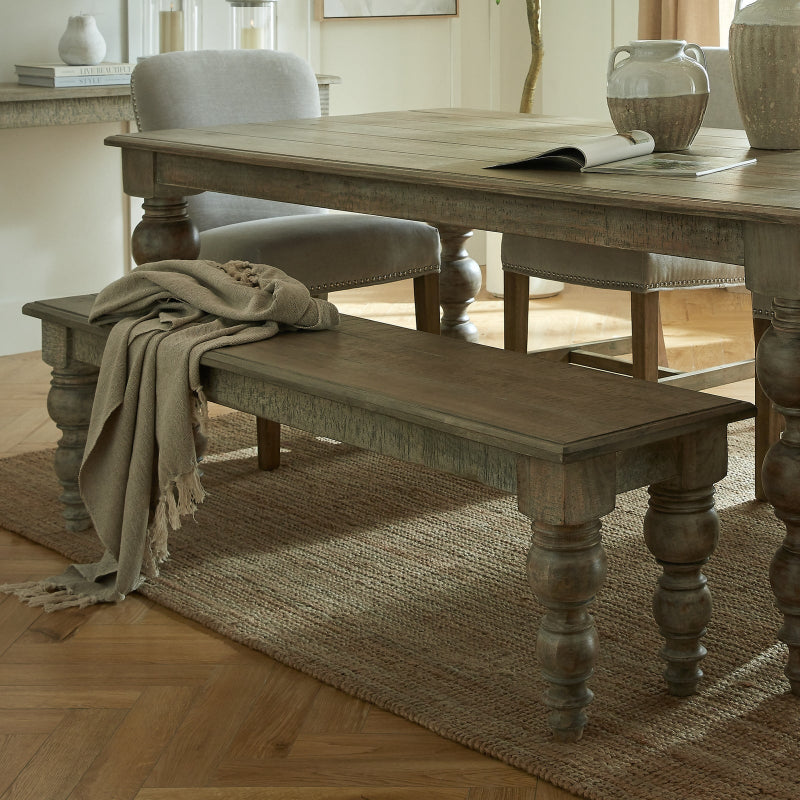 Wooden dining table with bench and chair in a room with light-colored walls and wooden flooring.