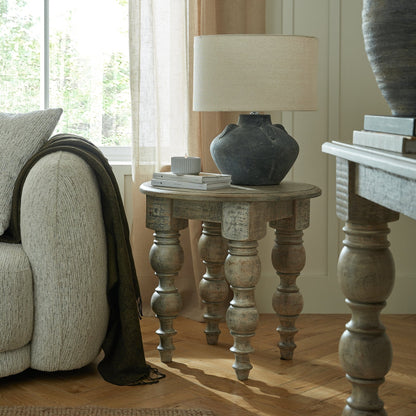 Wooden side table with lamp and books next to a sofa in a living room.