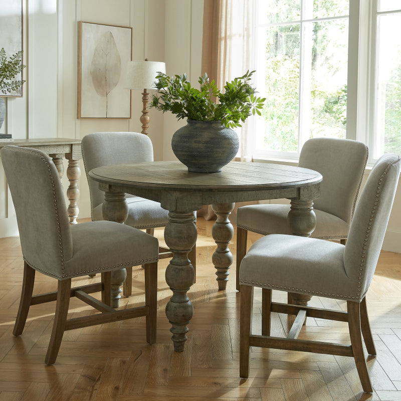 Round wooden dining table with four chairs in a bright room with large windows.