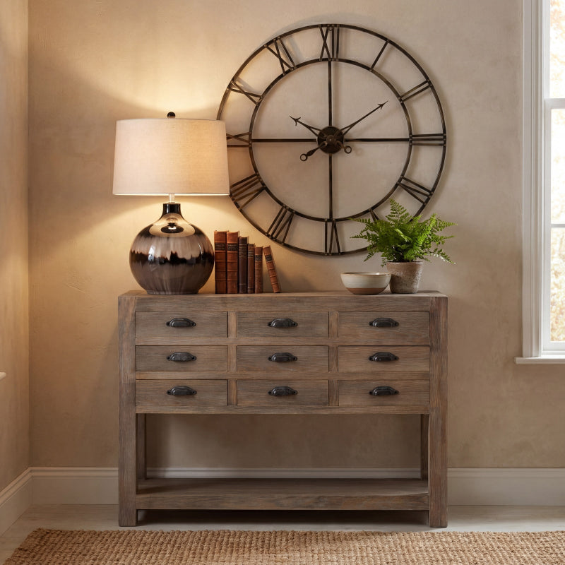 Wooden console table with lamp, books, and decorative items against a beige wall with a large wall clock.