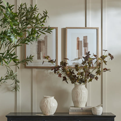 Decorative setting with framed art, vases, and plants on a wall.