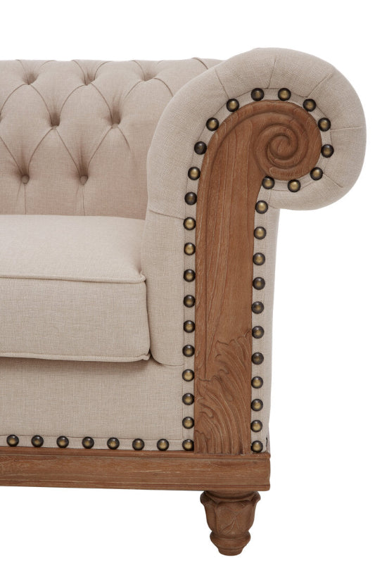 Beige tufted sofa with wooden armrest and decorative nailhead trim on a white background