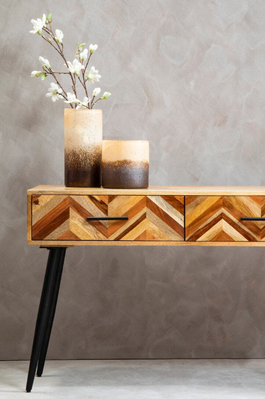 Wooden console table with chevron pattern and two decorative items on a plain background