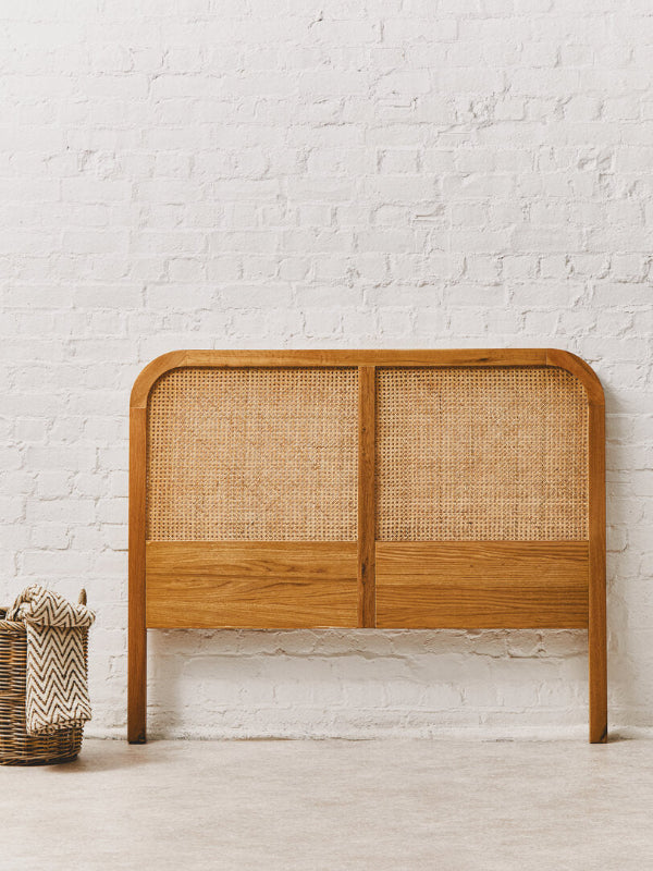 Wooden headboard with wicker panels against a white brick wall.