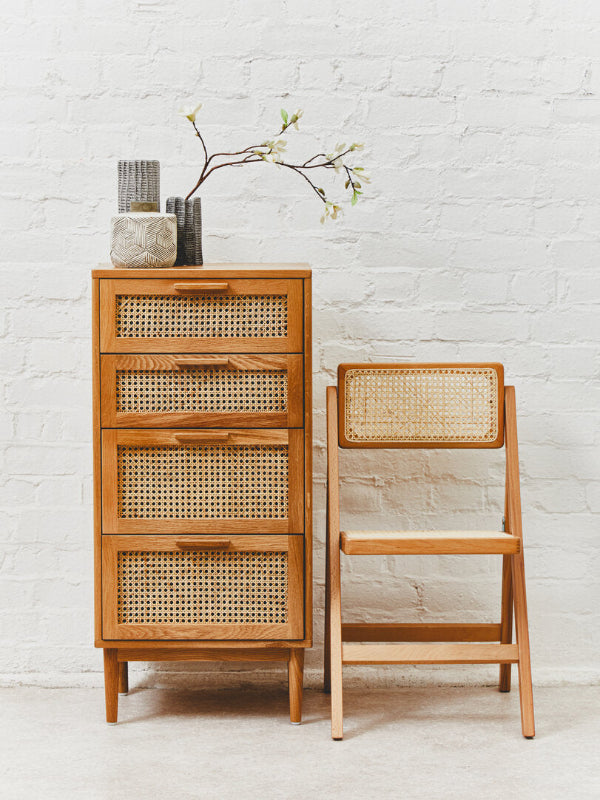 Wooden cabinet with wicker drawers and a matching chair against a white brick wall.