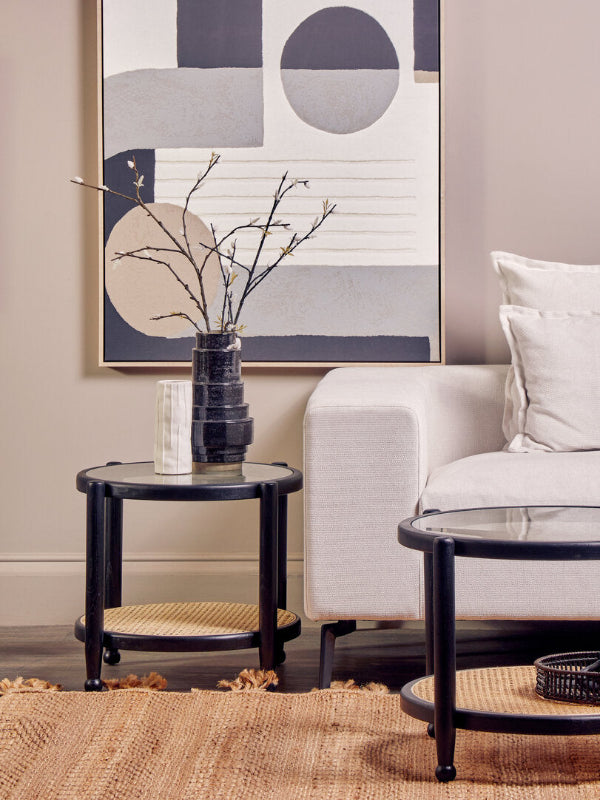 Modern living room with a white sofa, black side table, and abstract art on the wall.
