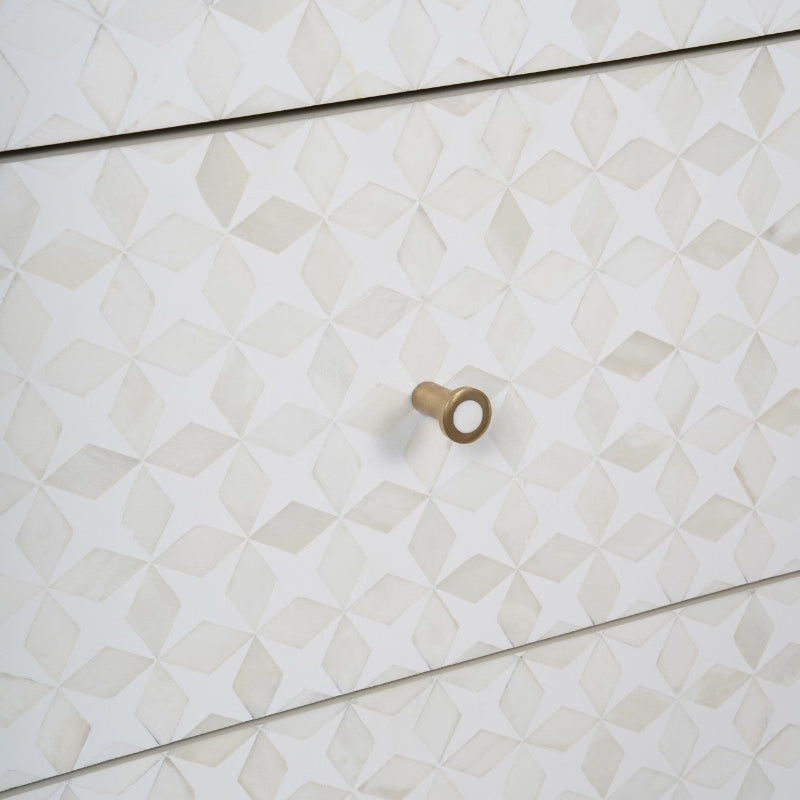 A close-up of a white dresser or cabinet with a geometric 3D diamond pattern on the drawer fronts and a single round brass knob.