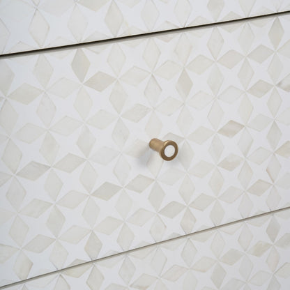 A close-up of a white dresser or cabinet with a geometric 3D diamond pattern on the drawer fronts and a single round brass knob.