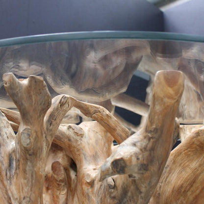 A close-up of a rustic driftwood table base with natural tan and brown wood textures under a clear glass tabletop.