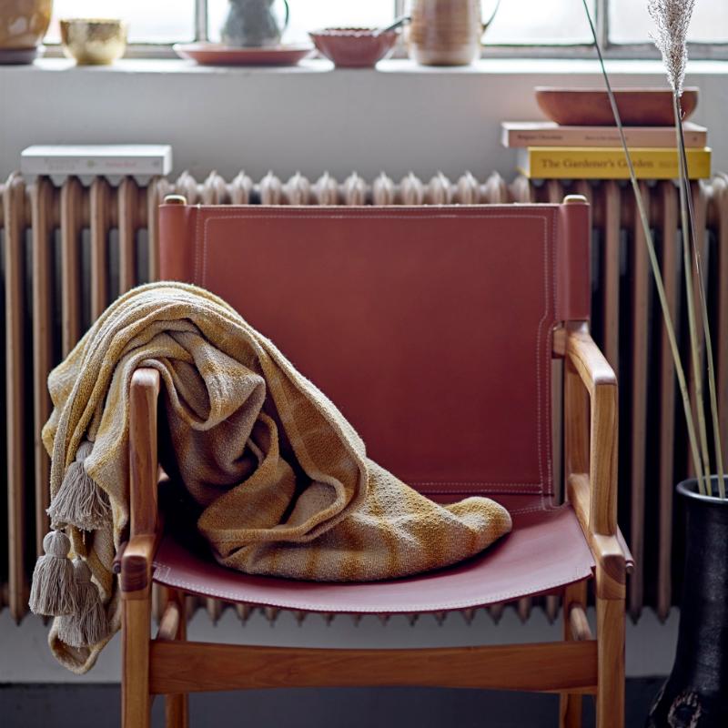 Pink chair with a beige blanket draped over it in a room with a radiator and window.