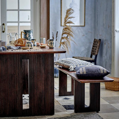 Dining room with wooden table, chairs, and decorative pillows on a patterned rug.