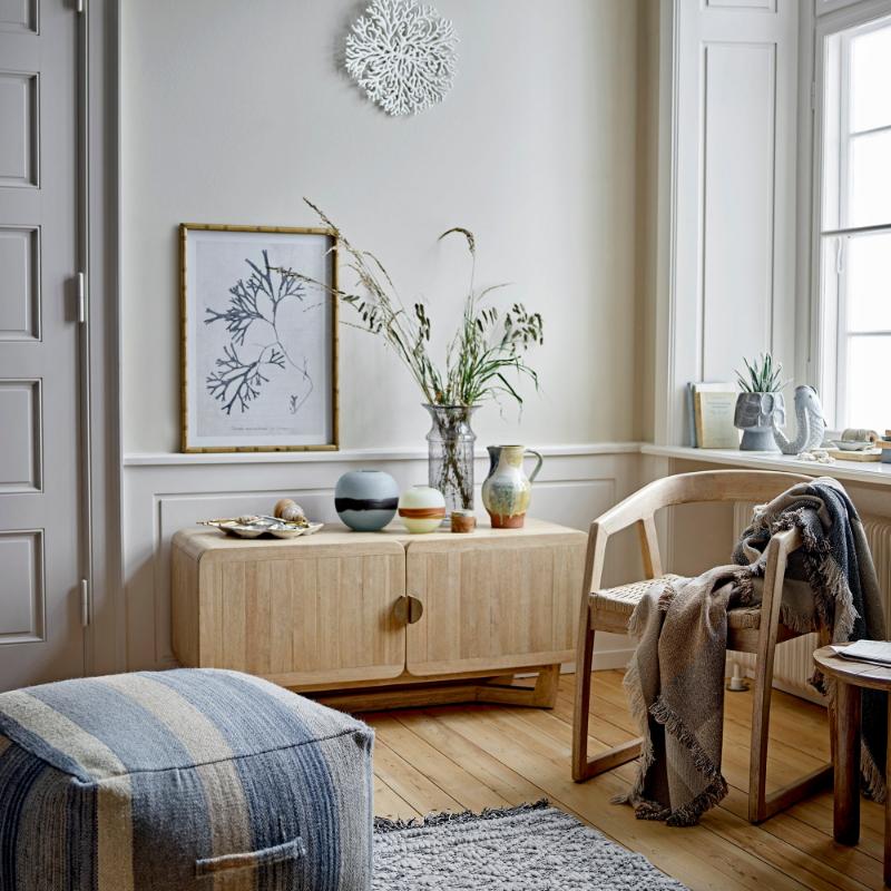 Nest living room with wooden sideboard, striped ottoman, and decorative elements.