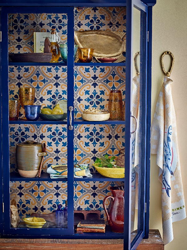 Blue cabinet with patterned back and glass doors displaying various items in a room.