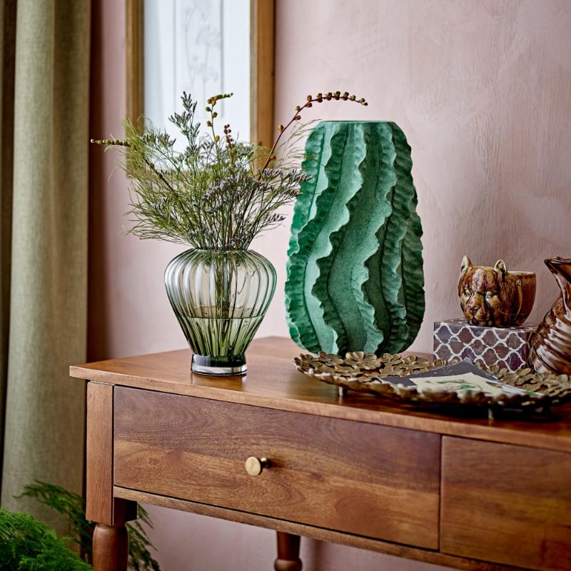 Decorative setting with a wooden console table, green vase, and framed artwork on a pink wall.