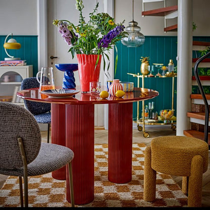 Dining room with a red table, chairs, and a staircase in the background.
