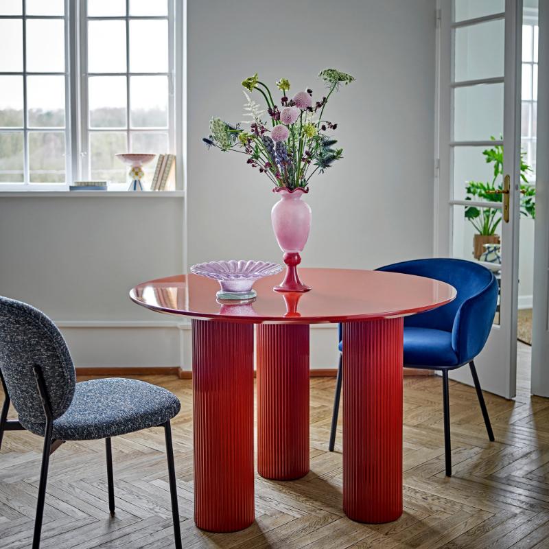 Modern dining room with a red table and chairs, featuring a vase with flowers.