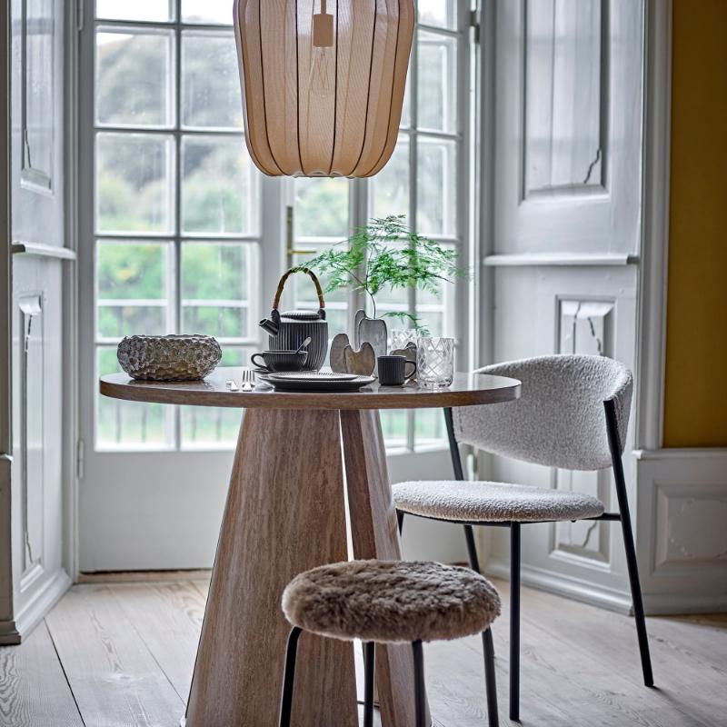 Dining area with wooden table, chair, and small stool in a bright room with large windows.