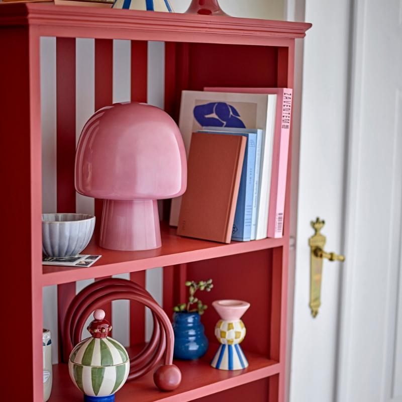 Pink bookshelf with decorative items against a striped wall