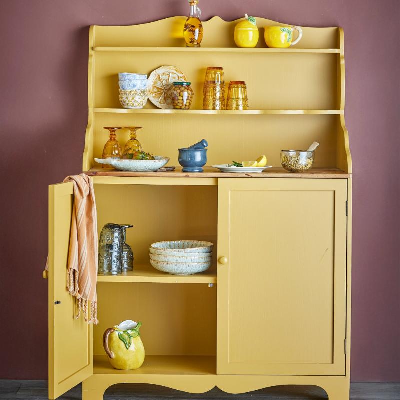 Yellow cabinet with various kitchen items against a purple wall