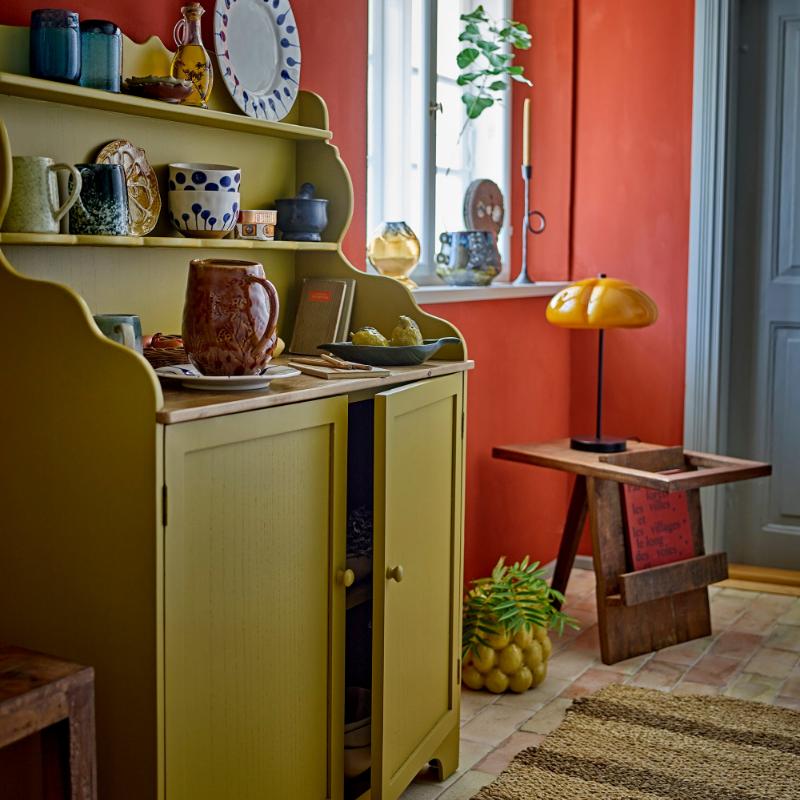Kitchen interior with a yellow cabinet, shelves with decorative items, and a red wall.