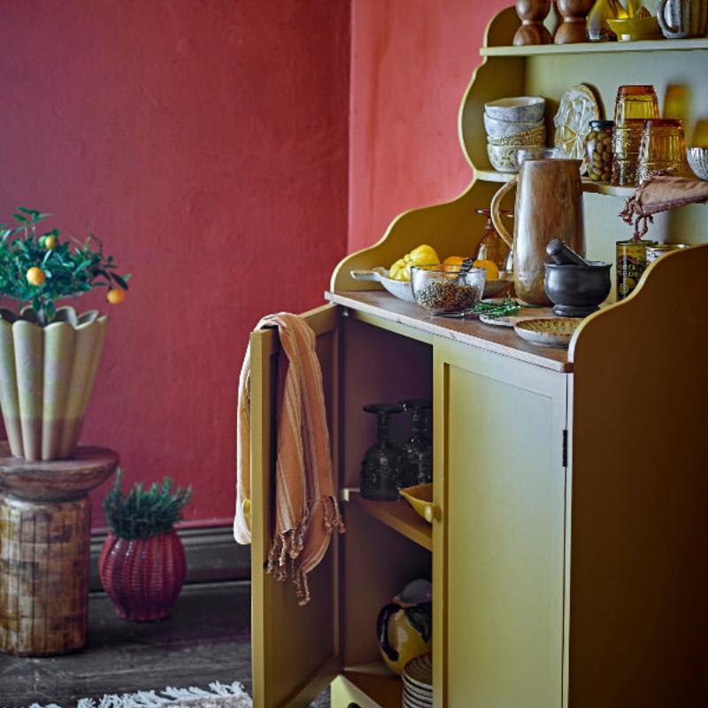 Yellow cabinet with open door displaying kitchen items against a red wall.
