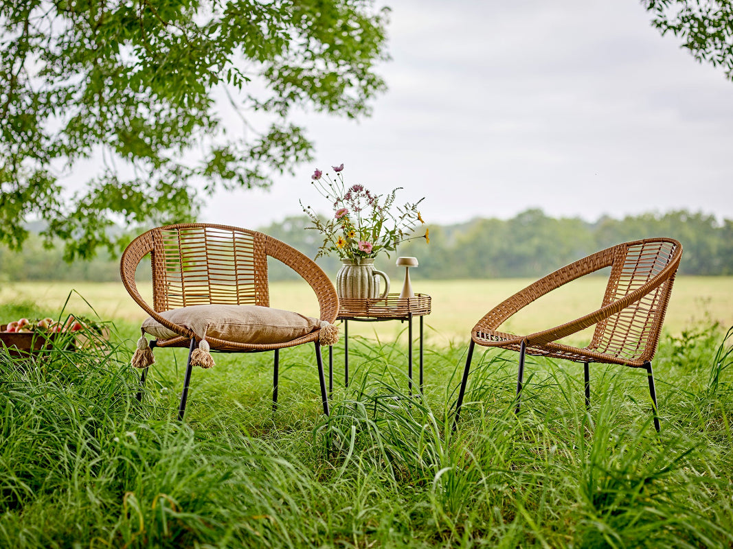Two wicker chairs and a small table with a teapot and flowers in a grassy field.