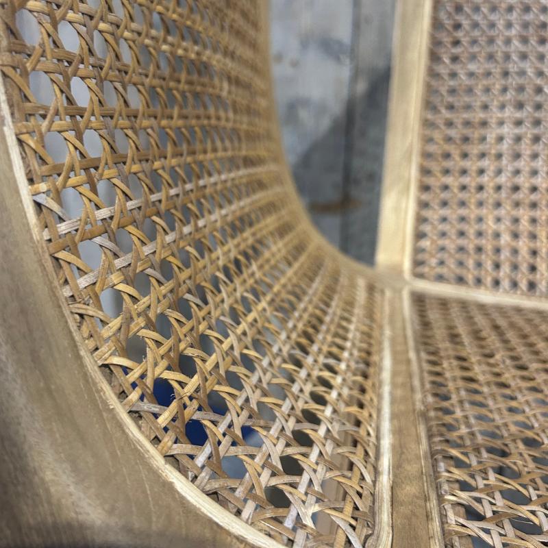 Close-up of a woven rattan chair back and seat with a light natural wood frame, showing the detailed texture of the cane weave.