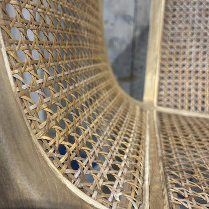 Close-up of a woven rattan chair back and seat with a light natural wood frame, showing the detailed texture of the cane weave.