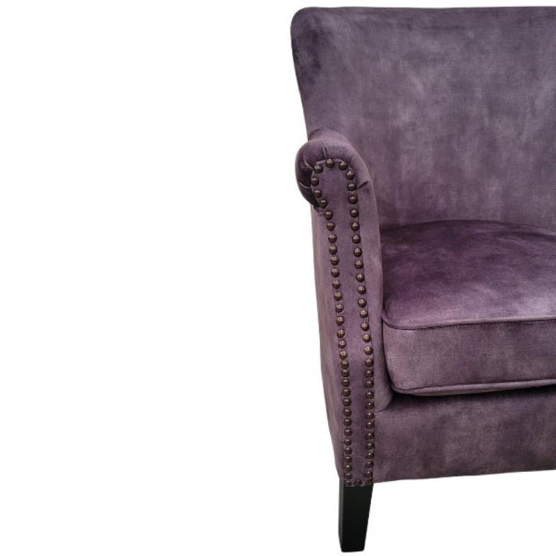 Close-up of a vintage charcoal velvet armchair with rolled arms, nailhead trim, and a dark wooden leg against a white background.