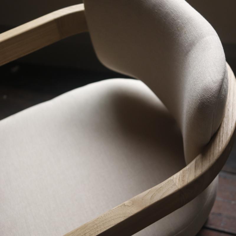 Close-up of a modern upholstered chair with a curved light wood frame and cream fabric seat and back cushion.