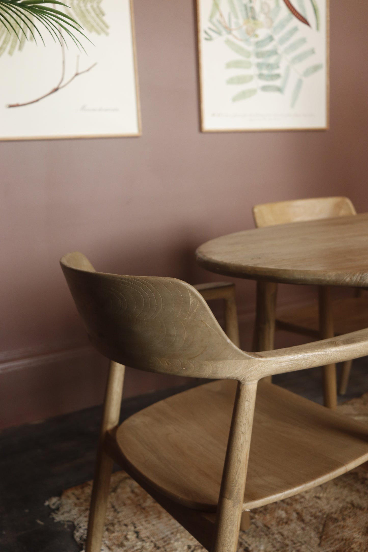 Wooden dining table and chairs against a mauve wall with framed artwork.