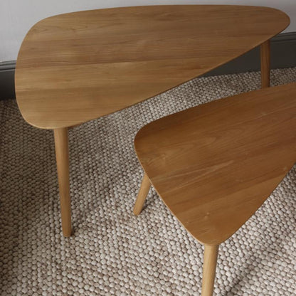 Two triangular wooden nesting tables with a light natural oak finish and tapered legs, shown on a textured beige woven rug.