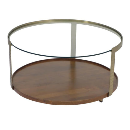 A round two-tier coffee table with a medium brown wooden bottom shelf, a clear glass top, and a brushed brass metal frame.